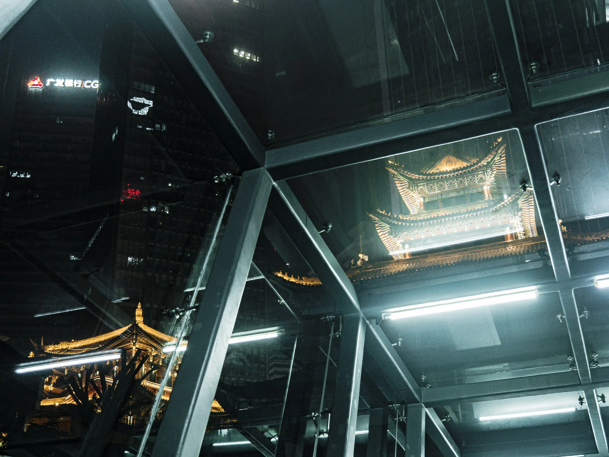 Reflections of a lit traditional roof inside a glass structure at night.
