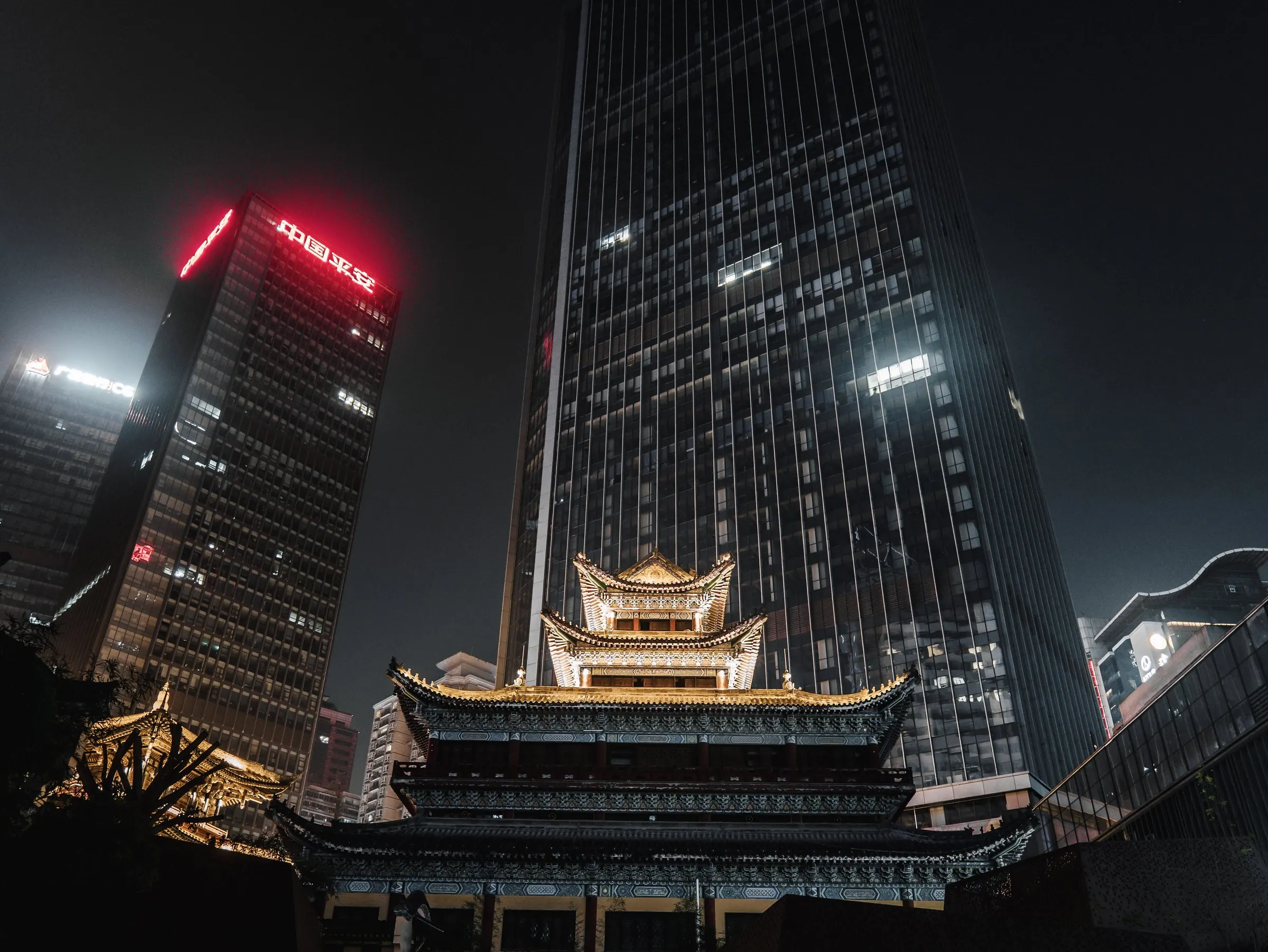 A traditional roof held against high-rise towers at night.