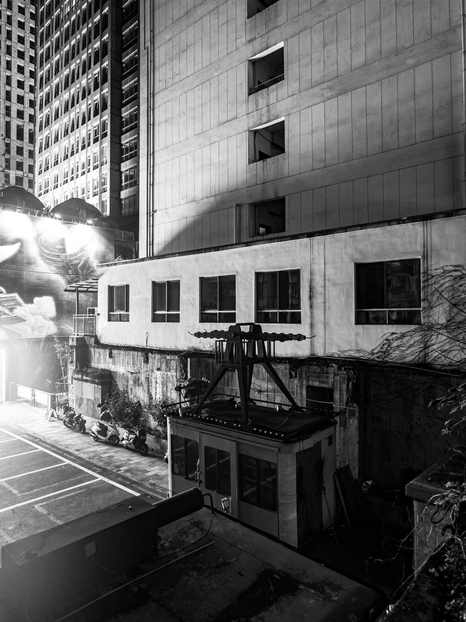 A black-and-white city wall and tower facade cut by harsh light at night.