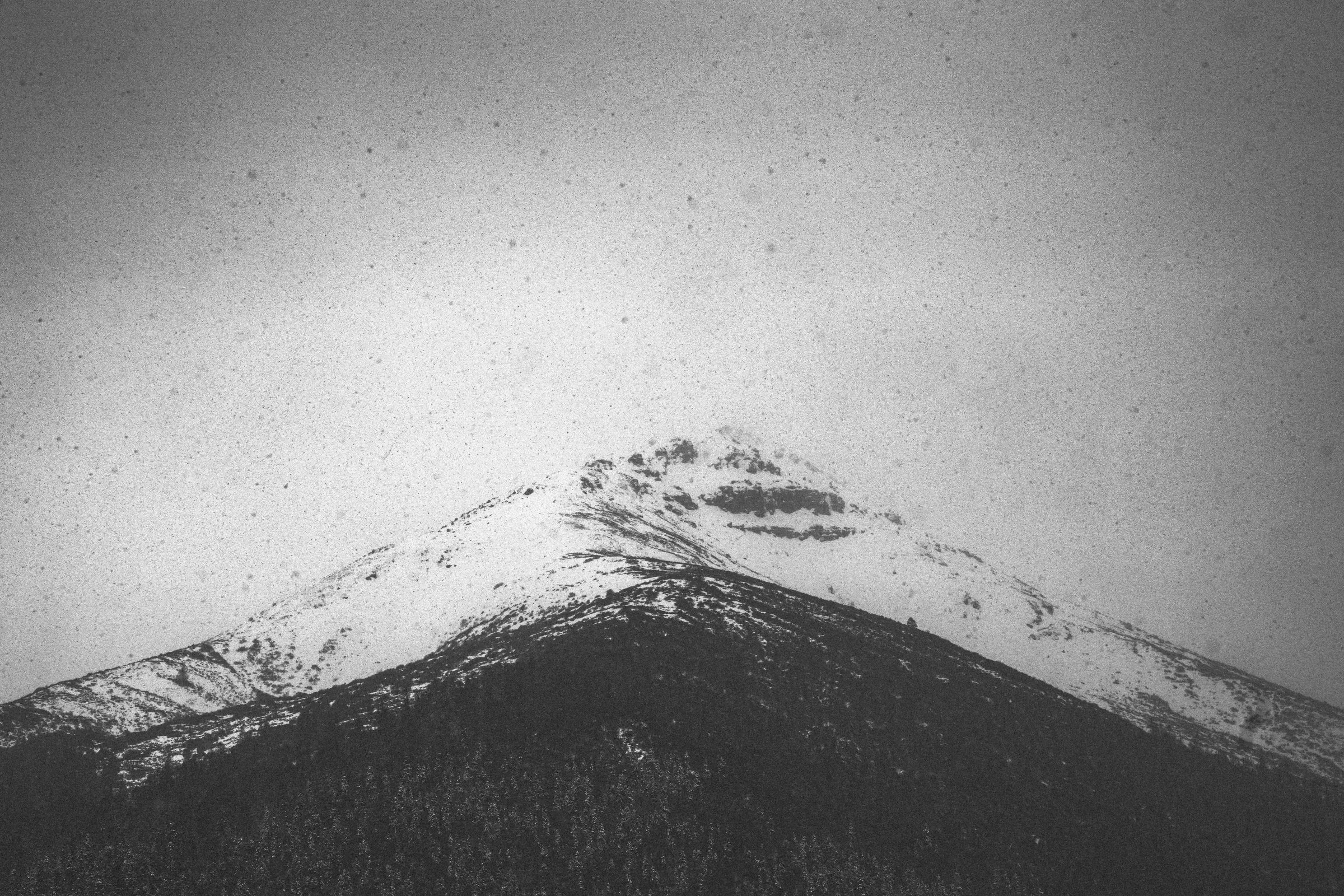 A monochrome snow ridge held above a dark mountain mass.