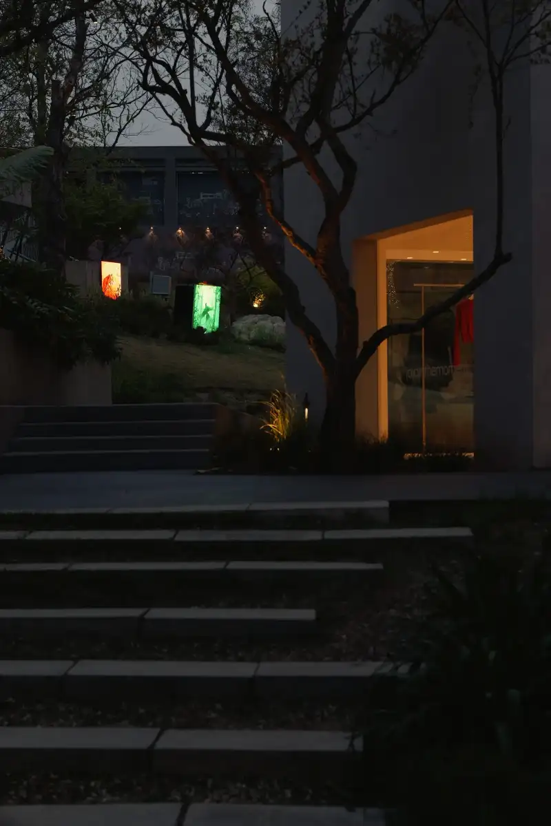 A dark exterior wall cut by tree branches and two glowing screens at night.