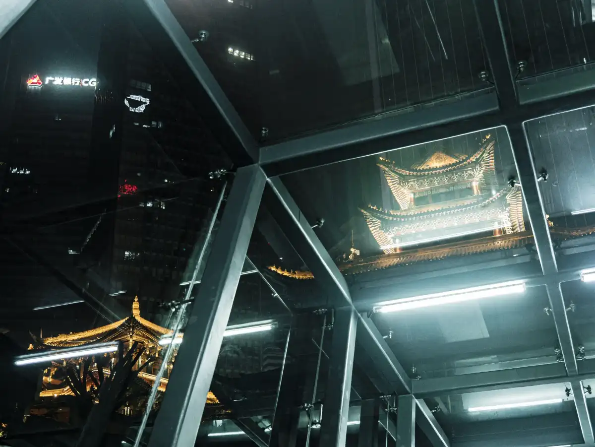 Reflections of a lit traditional roof inside a glass structure at night.