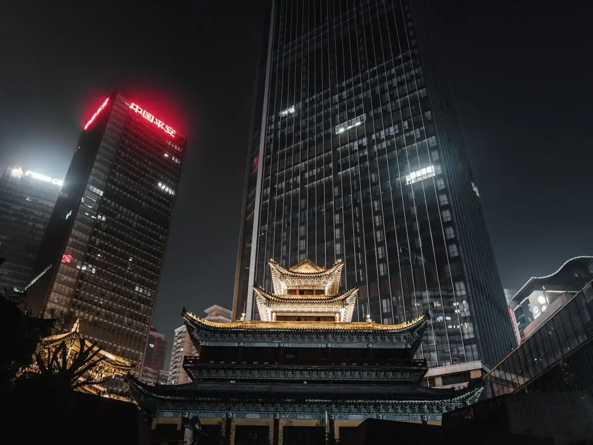A traditional roof held against high-rise towers at night.