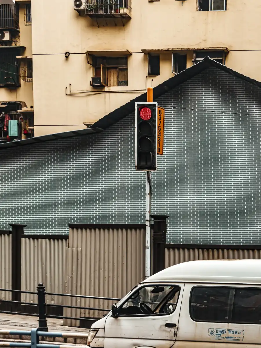 A red traffic light held between a tiled wall, an older building, and a passing van.